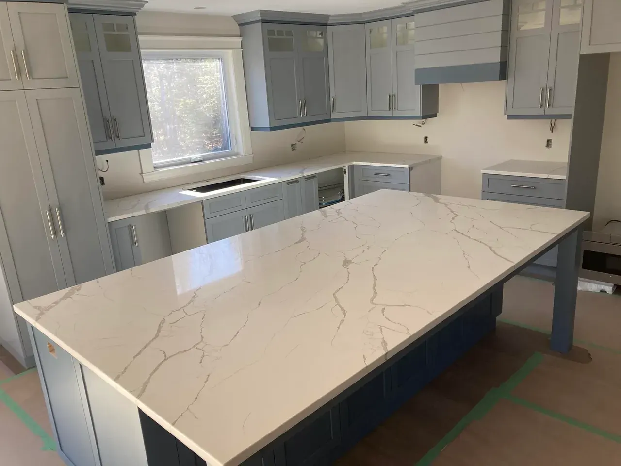Veined countertop island with blue-grey cabinets, a Prime Stone and Tile kitchen shown by Blueprint Cabinets